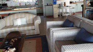 A living room with a sofa, armchair, and a coffee table. There is a kitchen area with a refrigerator, sink, and cabinets. - Kangela 11 (Ponta d'Ouro)
