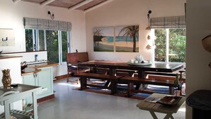A spacious kitchen with wooden benches, a dining table, and a view of the outdoors through large windows. - Kangela 11 (Ponta d'Ouro)