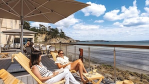 Una terraza de madera con sillas reclinables y sombrillas con vista a la playa.
