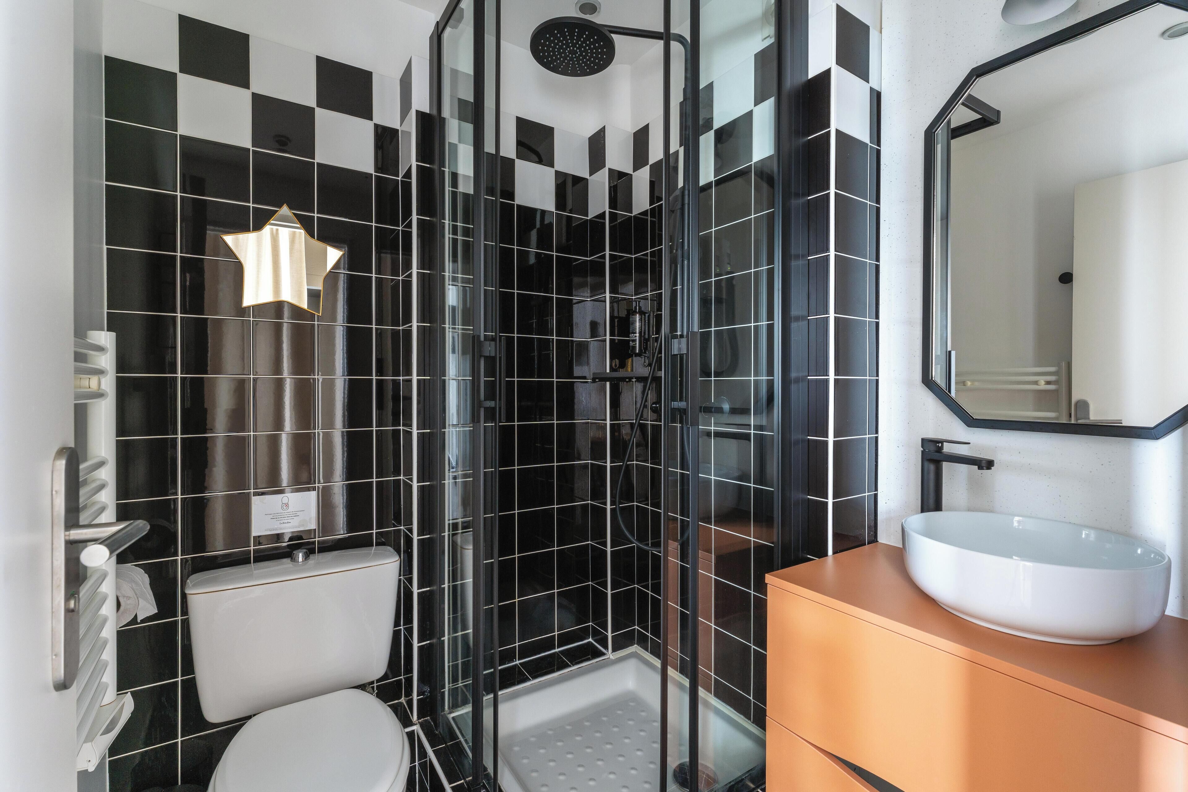 Ein modernes Badezimmer mit Wandverkleidung aus schwarz-weißen Schachfeldern, einer Glaskabine für die Dusche, einer weißen Toilette und einem großen, ovalen Waschbecken mit Spiegel darüber.