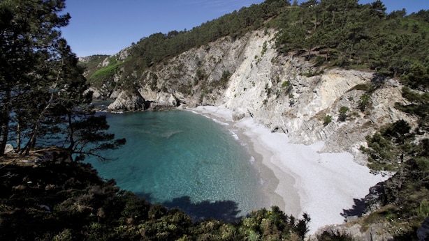 Paesaggio costiero con spiaggia sabbiosa, acque cristalline color turchese e scogliere rocciose.