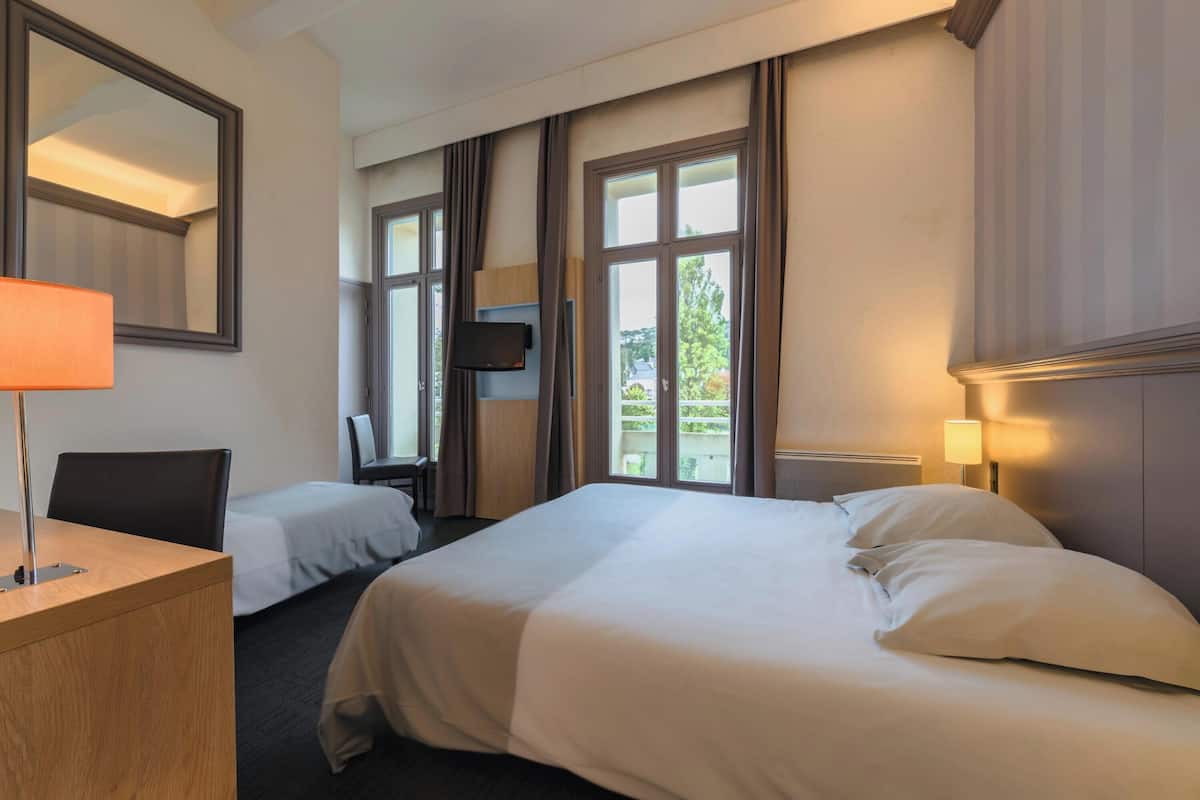 A hotel room with two beds, a desk, a chair, a TV, and a window with curtains.