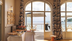 Zona pranzo con tavolo apparecchiato, ampie finestre con tende e vista sul mare.
