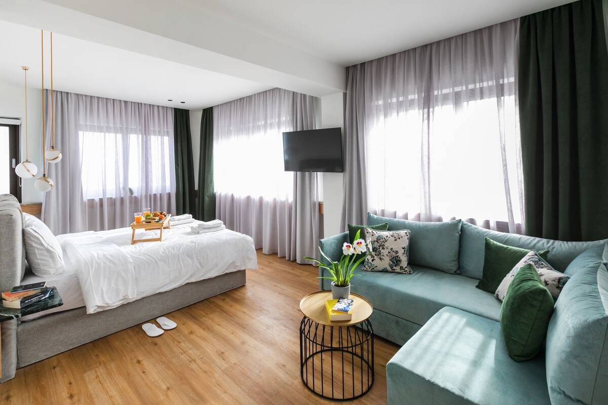 A modern hotel room with a bed, a sofa, a small round table with a plant, and a flat-screen TV.
