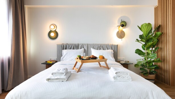 A hotel room with a neatly made bed, a tray with breakfast items, and a potted plant. - Septa Studios (Thessaloniki)