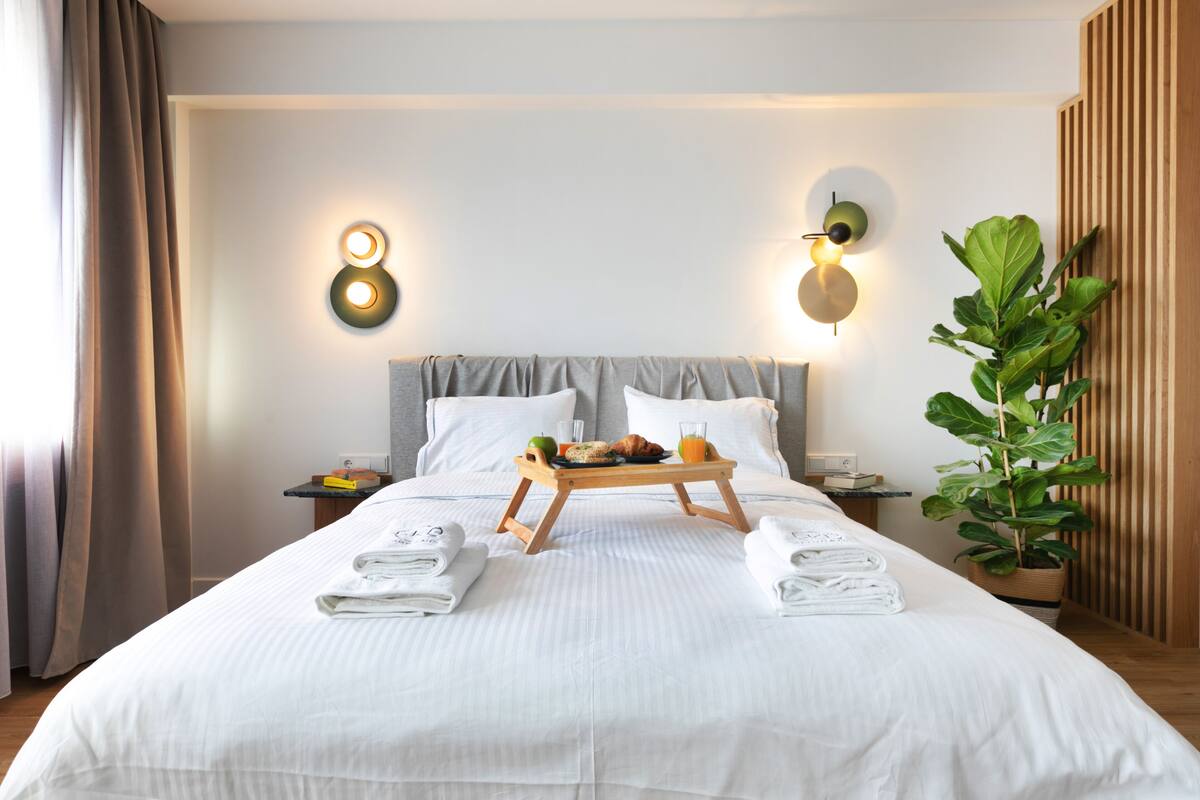 A hotel room with a neatly made bed, a tray with breakfast items, and a potted plant.