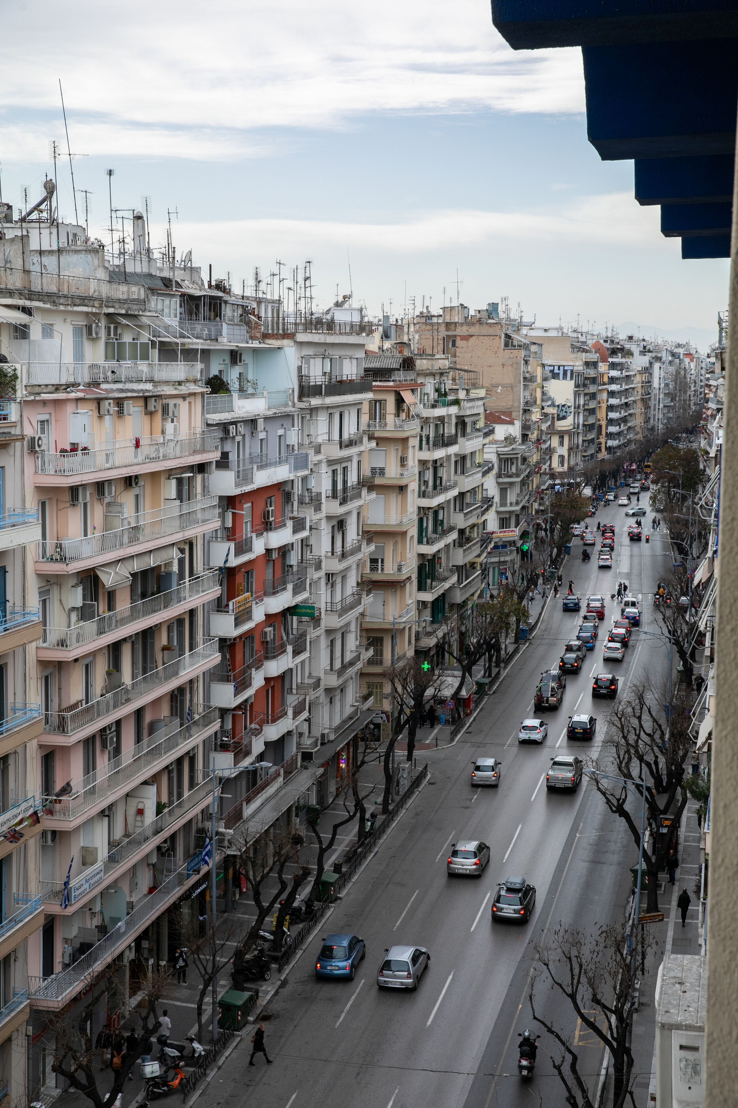 Un immeuble résidentiel à plusieurs étages, doté de balcons, situé dans une rue animée, avec des voitures garées.