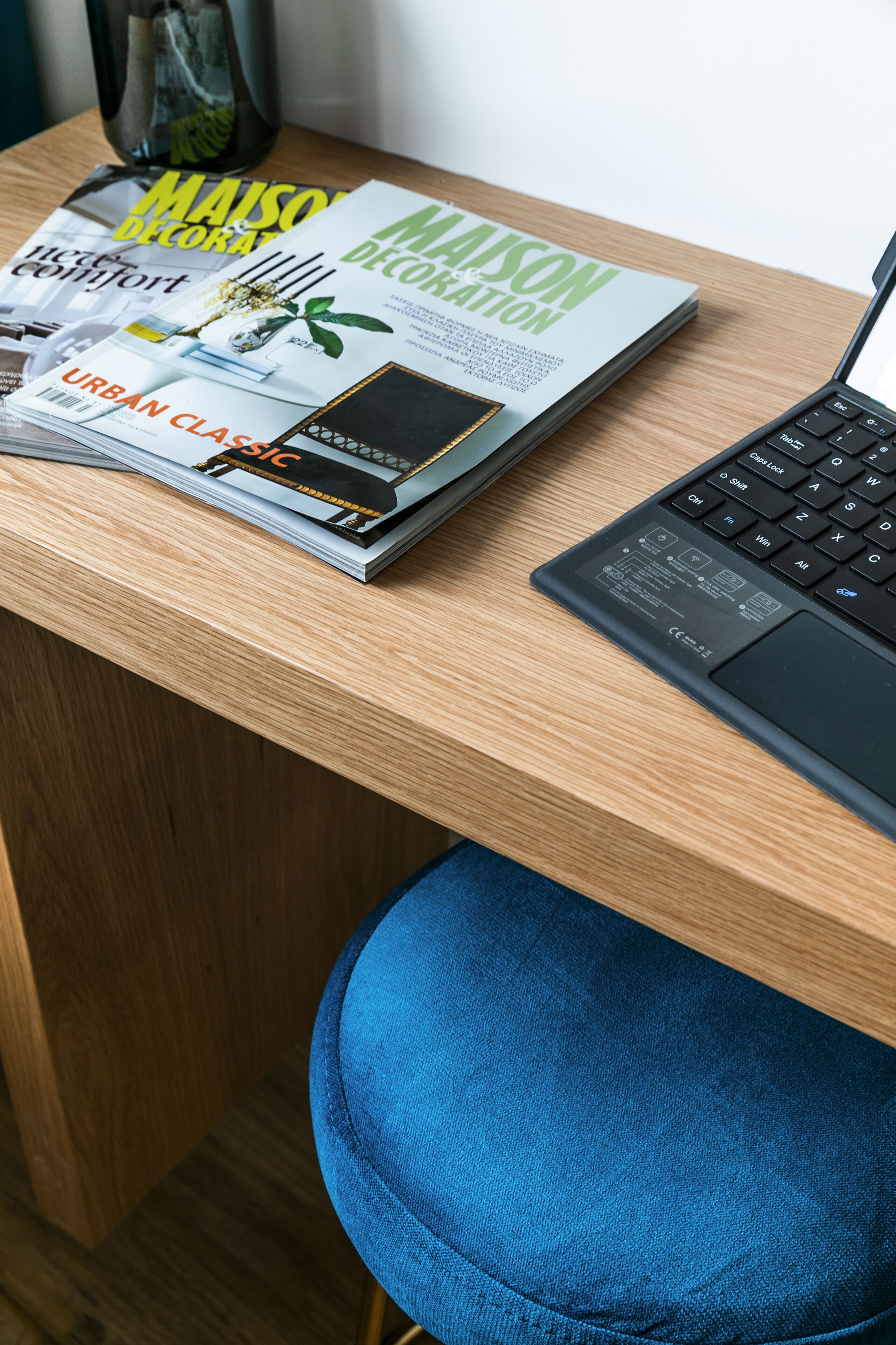 Un bureau en bois avec un ordinateur portable, une pile de magazines et une chaise bleue.