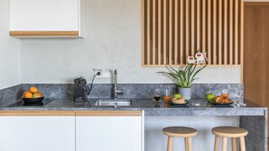 A modern kitchen with a marble countertop, a sink, and wooden stools. - Septa Studios (Thessaloniki)