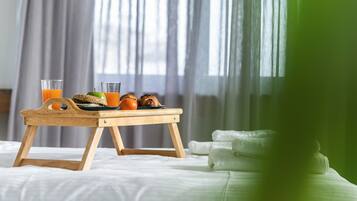 Un lit avec un plateau en bois sur lequel se trouvent des aliments pour le petit-déjeuner, un verre de jus d’orange et une pomme verte.