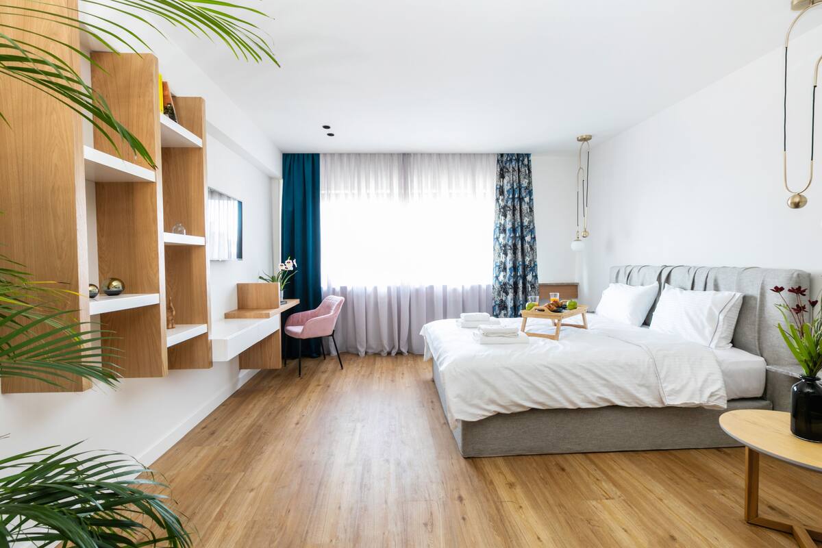 A modern hotel room with a bed, a desk, a chair, and built-in wooden shelves.