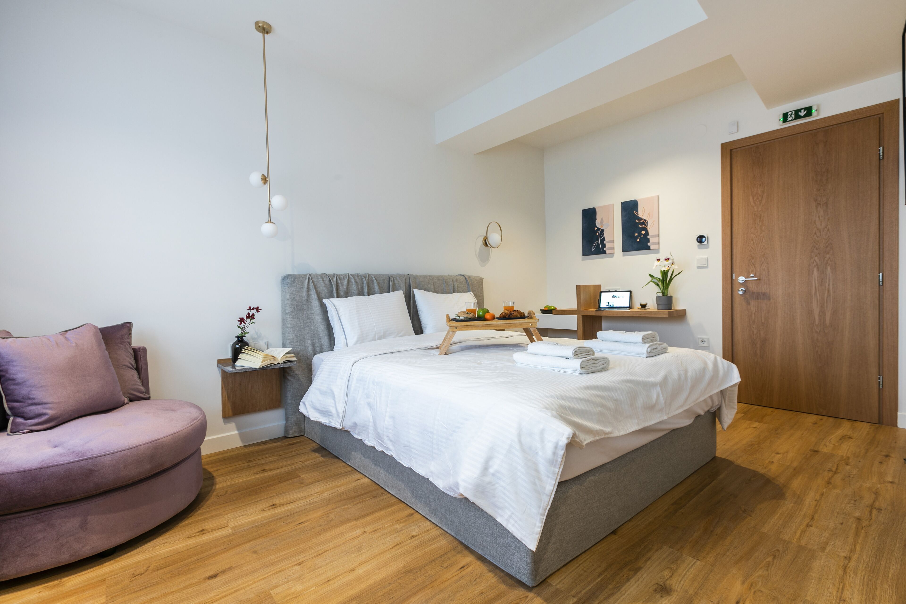 A modern bedroom with a bed, a bedside table, a nightstand, a wooden wardrobe, a sofa, and a hanging light fixture.