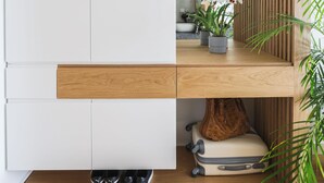 A modern bathroom with a wooden vanity, a sink, and a mirror. There are shoes and a suitcase under the vanity. - Septa Studios (Thessaloniki)