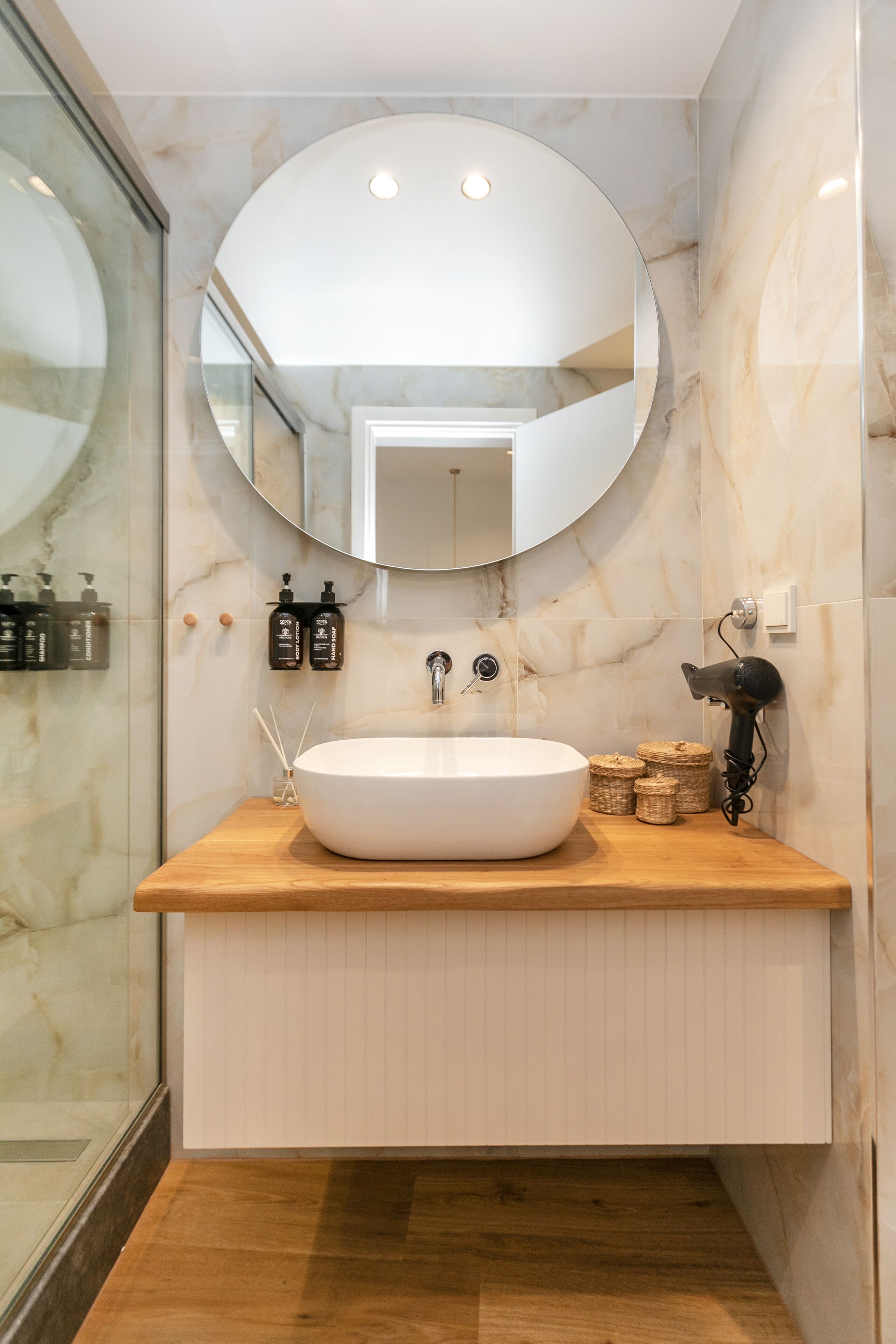 Une salle de bain avec un lavabo blanc, un miroir rond et un sèche-cheveux fixé au mur.