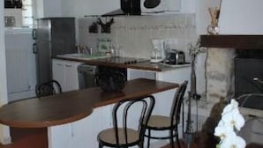 A compact kitchen with a central island, a dining area with chairs, and a fireplace. - GITE AUX FLEURS DE CERISES - Le Plessis Luzarches (95) _ 4 people (Le Plessis-Luzarches)