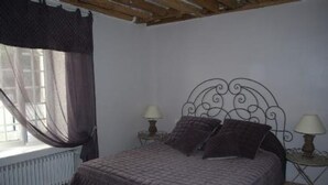 A bedroom with a bed, two bedside tables with lamps, a window with curtains, and a radiator. - GITE AUX FLEURS DE CERISES - Le Plessis Luzarches (95) _ 4 people (Le Plessis-Luzarches)