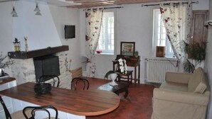 A cozy living room with a fireplace, a dining table, and a sofa. - GITE AUX FLEURS DE CERISES - Le Plessis Luzarches (95) _ 4 people (Le Plessis-Luzarches)