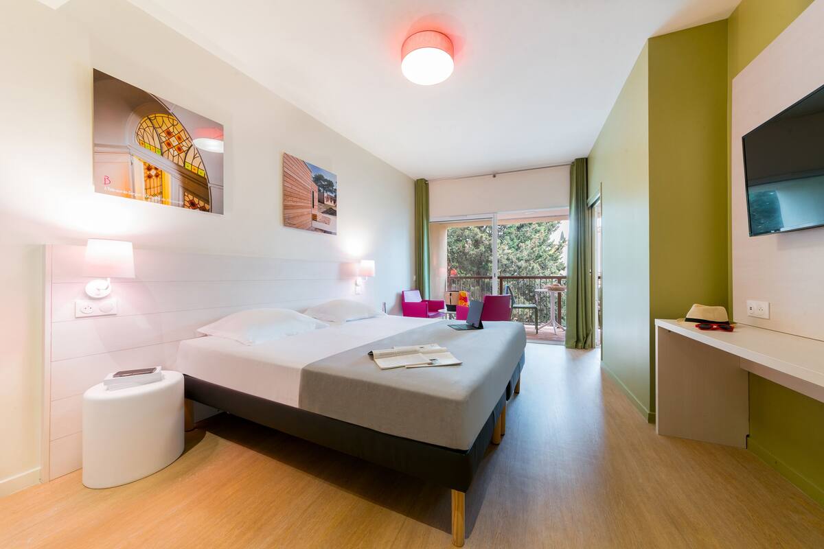 Une chambre d’hôtel moderne équipée d’un lit, d’une table de chevet et d’un téléviseur fixé au mur.