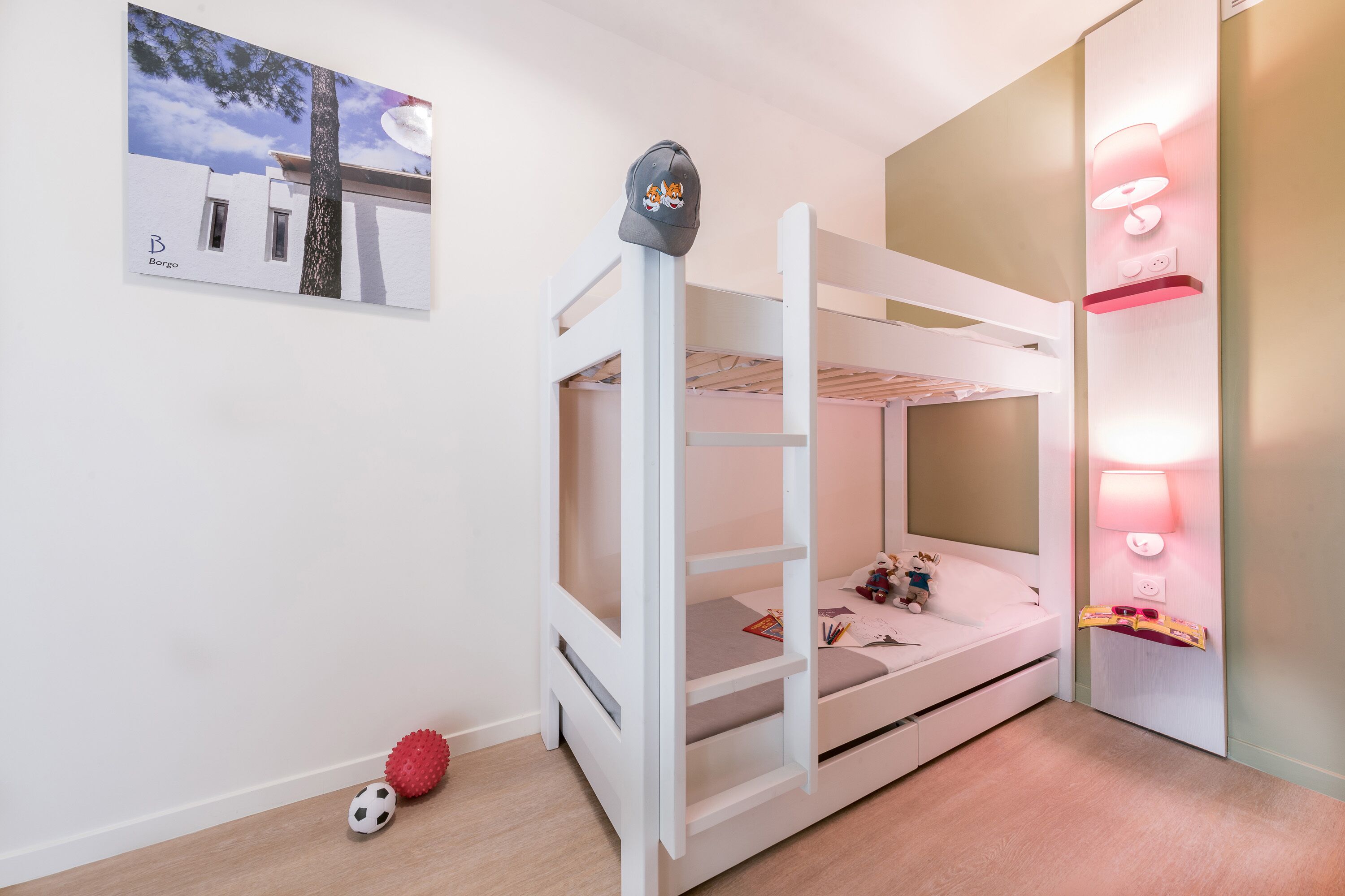 A bunk bed room with a white color scheme, a wall-mounted lamp, and a framed picture on the wall.