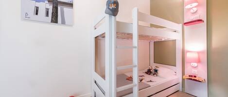 A bunk bed room with a white color scheme, a wall-mounted lamp, and a framed picture on the wall.