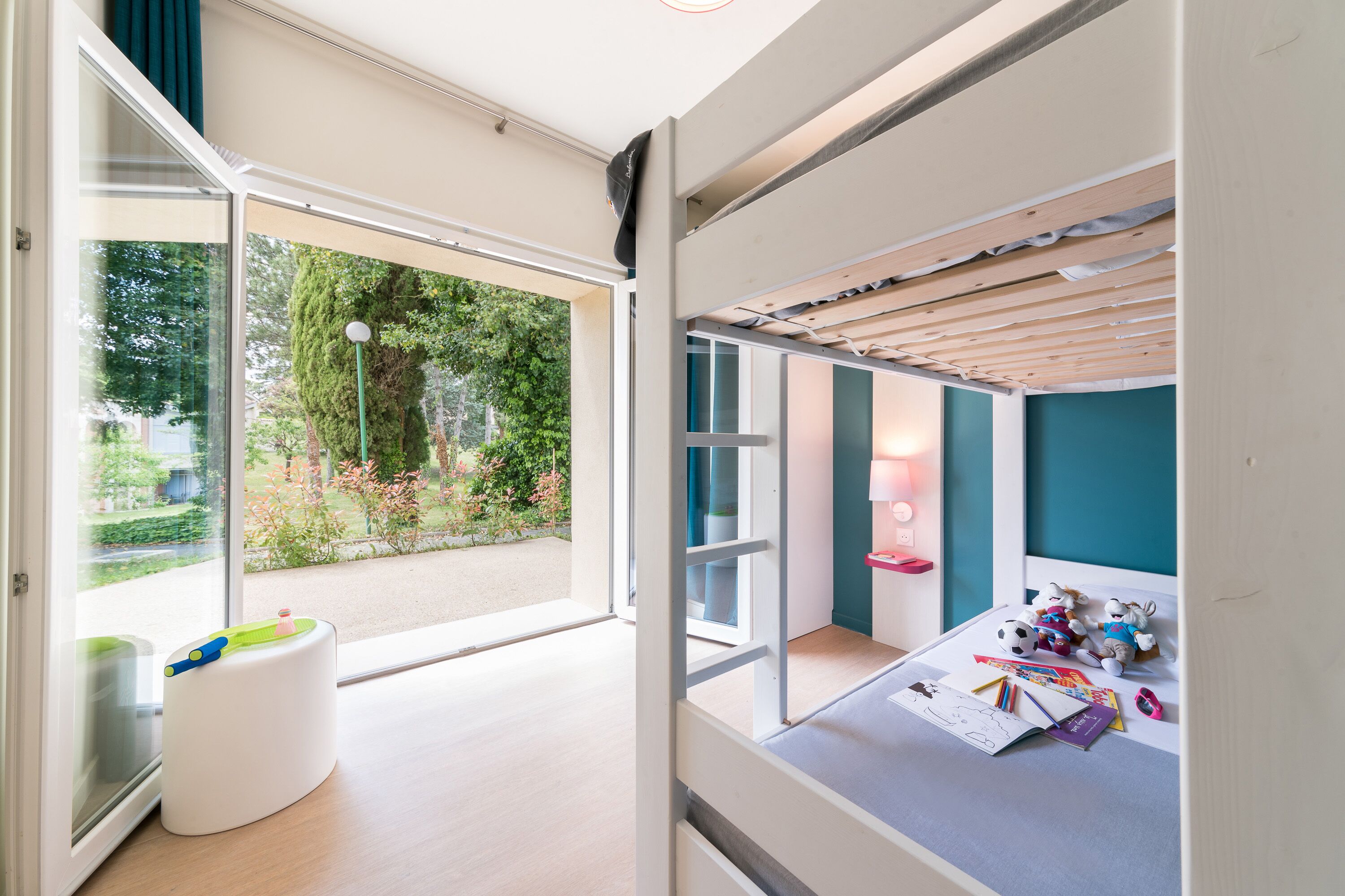 A modern child's room with a large window, a white playpen, and a bed with stuffed animals.
