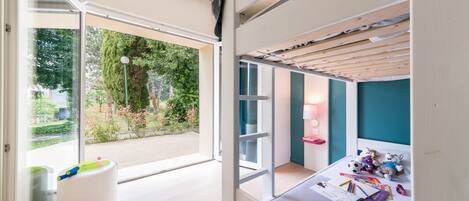 A modern child's room with a large window, a white playpen, and a bed with stuffed animals.