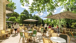 Un patio al aire libre con sillas y mesas de mimbre, sombrillas y vistas a árboles y un edificio al fondo.