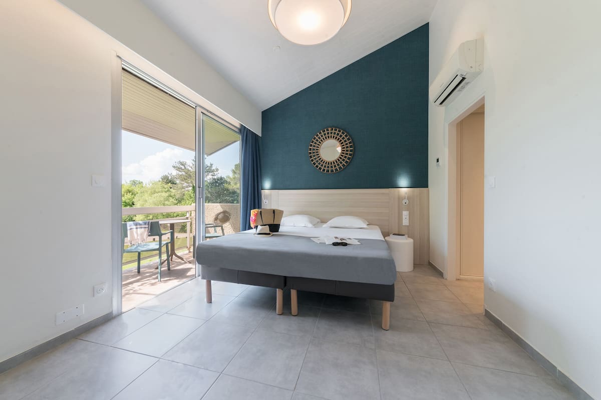 Une chambre moderne avec un lit, un miroir rond et une vue sur l’extérieur.