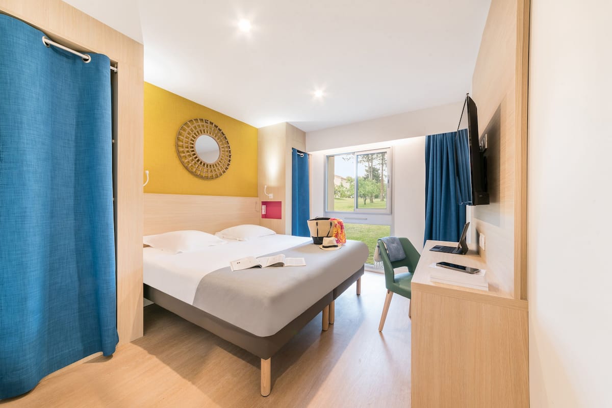 Une chambre d’hôtel moderne équipée d’un lit, d’un bureau avec un ordinateur portable, d’une télévision et offrant une vue sur l’extérieur.