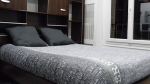 Une chambre à coucher avec un lit, une tête de lit en bois foncé, des étagères intégrées et une grande fenêtre.