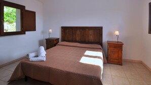 A bedroom with a large bed, two nightstands, a wooden headboard, and a window with a view of greenery. - Residence a Badesi ID 3372 (Badesi)