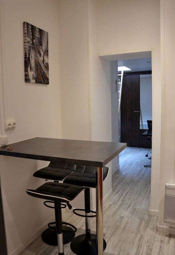 A narrow hallway with a black bar stool and a table. A painting is on the wall.