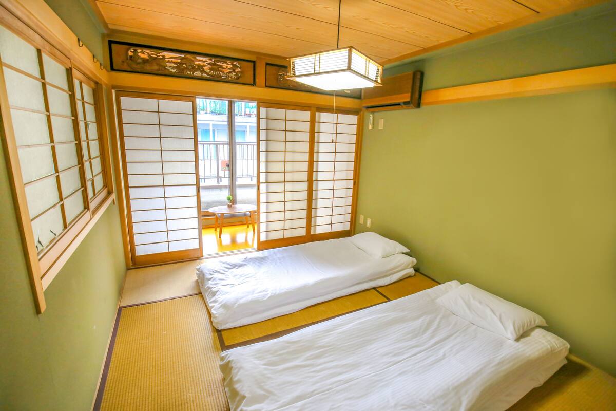 A traditional Japanese room with tatami flooring, a low bed with white bedding, and sliding shoji doors.