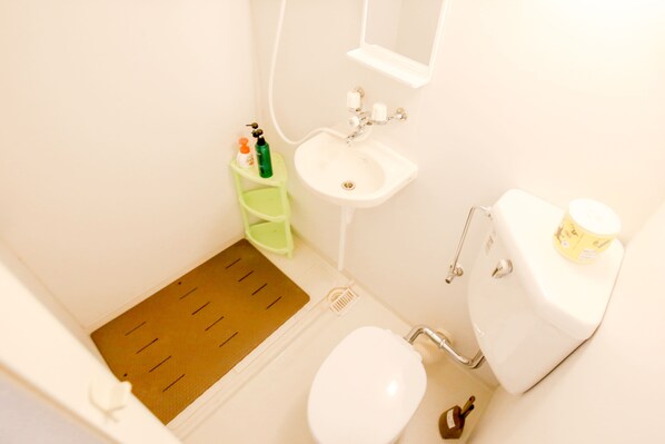 A small bathroom with a toilet, sink, and shower. There is a green step stool next to the sink. - Shinsaibashi Qilv Apartments (Osaka)