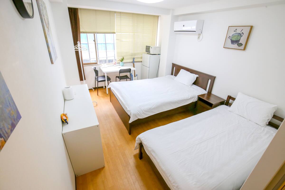 A hotel room with two beds, a desk, a chair, and a window with blinds.