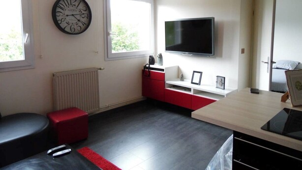Ein modernes, helles Zimmer mit einer großen Uhr, einem Flachbildfernseher und einem roten Schrank.