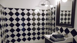 Ein Badezimmer mit Wand aus schwarz-weißen Rautenfliesen, einer weißen Badewanne und einem schwarzen Waschbecken mit Spiegel darüber.