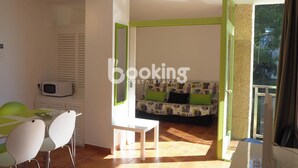A room with a dining area, a sofa with cushions, a microwave, and a view through an open door. - COZY APARTMENT WITH AIR CONDITIONING & COMMUNAL SWIMMING POOL IN LOS PINOS (Platja d'Aro)