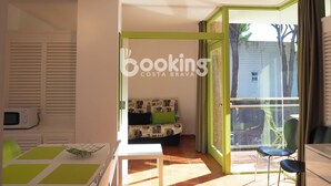 A modern living room with a sofa, a dining table, and a large window. - COZY APARTMENT WITH AIR CONDITIONING & COMMUNAL SWIMMING POOL IN LOS PINOS (Platja d'Aro)