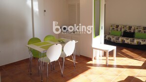 A dining area with a white table and four green chairs, a small white table, and a sofa with green cushions in the background. - COZY APARTMENT WITH AIR CONDITIONING & COMMUNAL SWIMMING POOL IN LOS PINOS (Platja d'Aro)