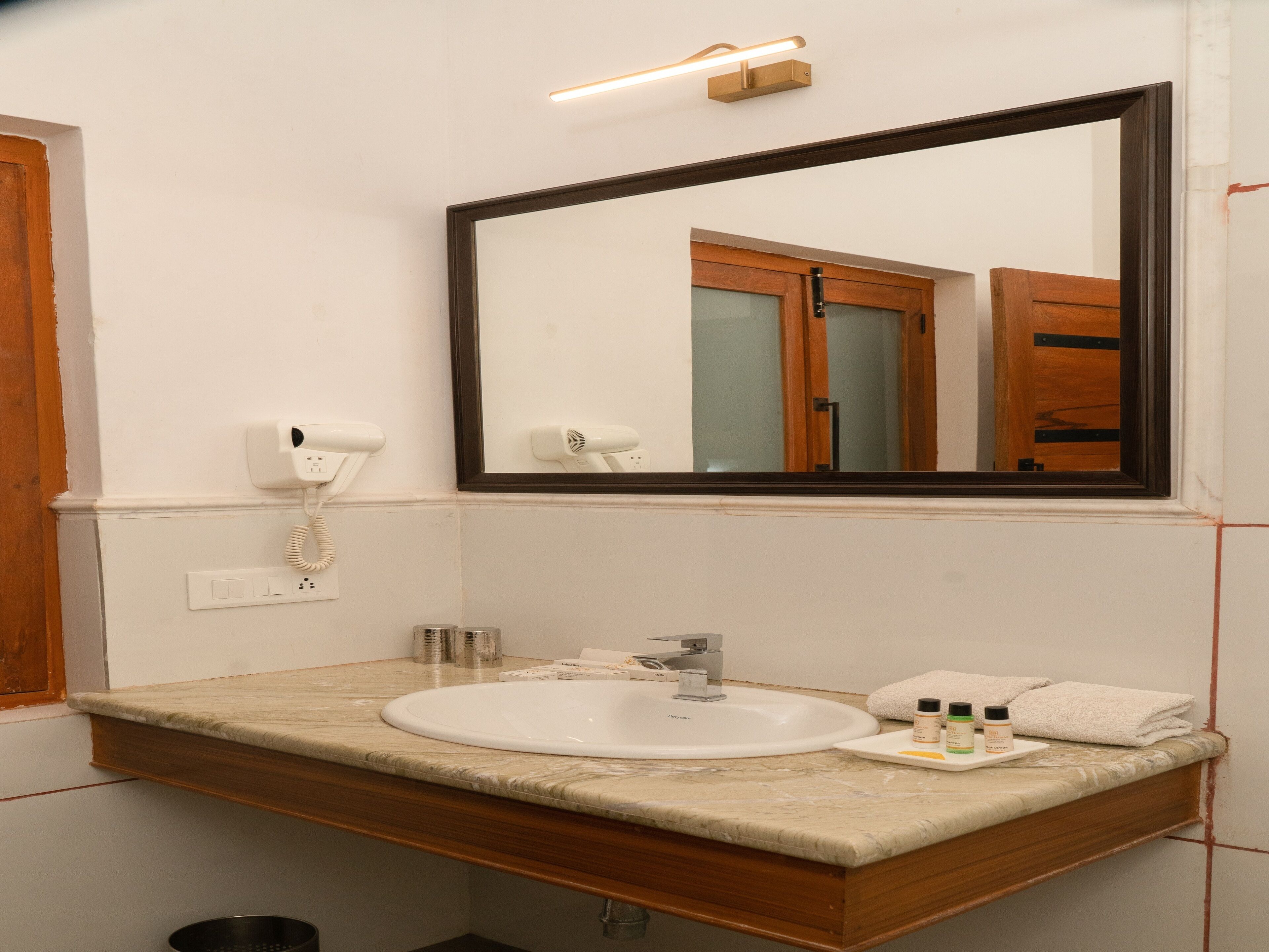 Une salle de bain avec un lavabo blanc, un miroir, un sèche-cheveux et un porte-serviettes.