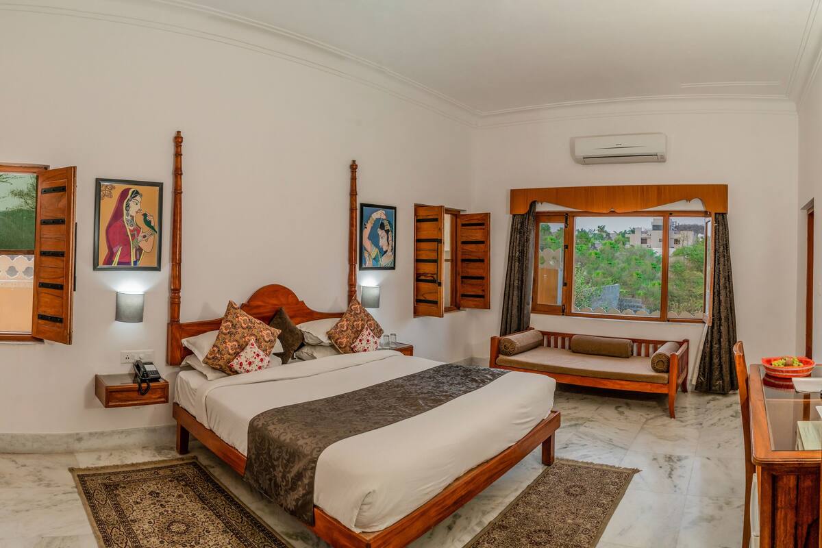 A well-lit bedroom with a large bed, wooden furniture, and artwork on the walls.