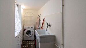 Uma lavanderia com máquina de lavar, pia e janela com cortinas.