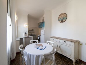 A compact kitchen with a dining area, featuring a round table, chairs, a white cabinet, and a clock on the wall.