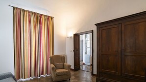 Um quarto com uma poltrona bege, um guarda-roupa de madeira e uma cortina listrada e colorida.