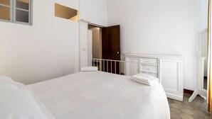 Quarto com cama, guarda-roupa branco e porta que dá para outro espaço.