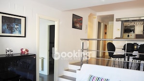 Een moderne woonkamer met een bank, een glazen salontafel en een keuken die zichtbaar is door een open deur.