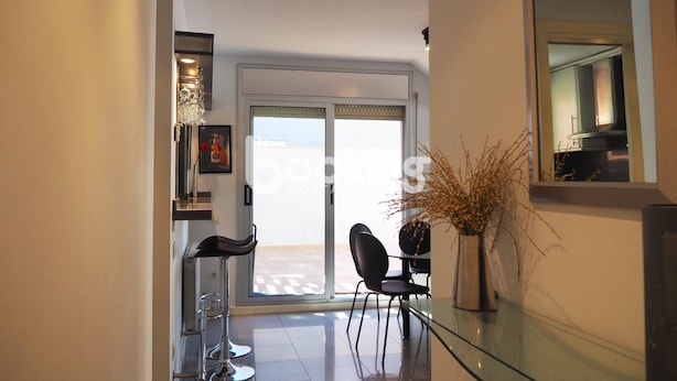 Een modern interieur met een eettafel met glazen blad, zwarte stoelen, een hoge barkruk en een vaas met gedroogde planten.