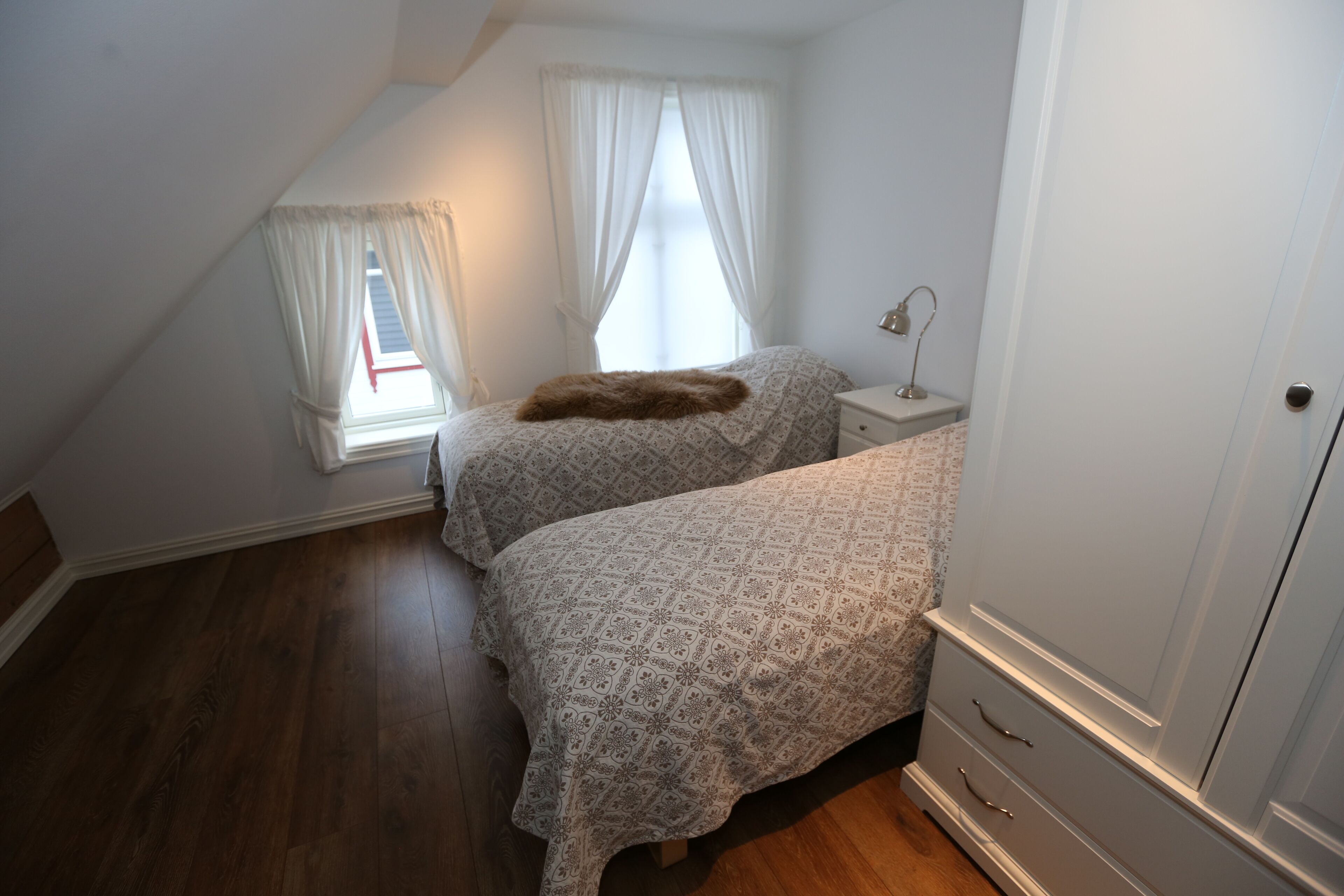 Un dormitorio con techo inclinado, una cama con ropa de cama estampada, una mesita de noche con lámpara y un armario.