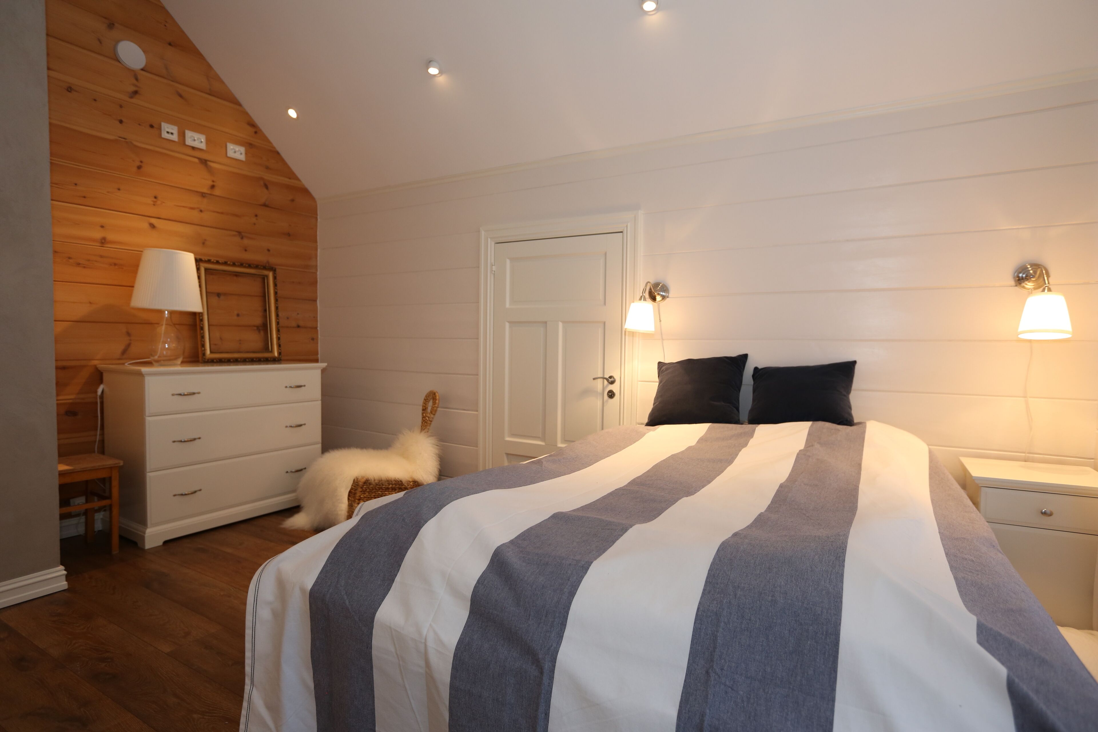 Un dormitorio con una cama grande, paredes de madera, un aparador blanco y dos lámparas de noche.